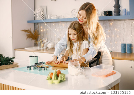 Family preparation of ginger biscuits with daughter. Mother and little girl cooking cookies. Blonde woman wearing blue shirt and girl white t-shirt. 133555135