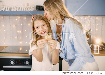 Blonde woman and her daughter holding a homemade ginger biscuits. Family preparation of ginger biscuits with child. Mother and daughter cooking cookies. Blonde woman and her daughter holding a homemade ginger biscuits. Family preparation of ginger biscuits with child. Mother and daughter cooking cookies. 133555137