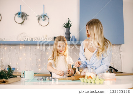 Family preparation of ginger biscuits with daughter. Mother and little girl cooking cookies. Blonde woman wearing blue shirt and girl white t-shirt. 133555138