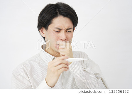 Man in his 20s measuring his temperature with a thermometer, white background 133556132