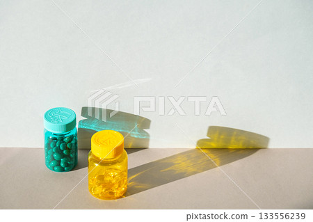 Two plastic bottles, one teal with green pills and one yellow with clear capsules Two plastic bottles, one teal with green pills and one yellow with clear capsules 133556239