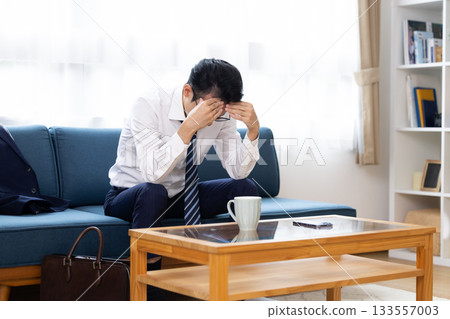 Man sitting on sofa holding his head Man sitting on sofa holding his head 133557003