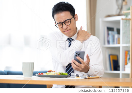 A man eating while looking at his smartphone before going to work A man eating while looking at his smartphone before going to work 133557556