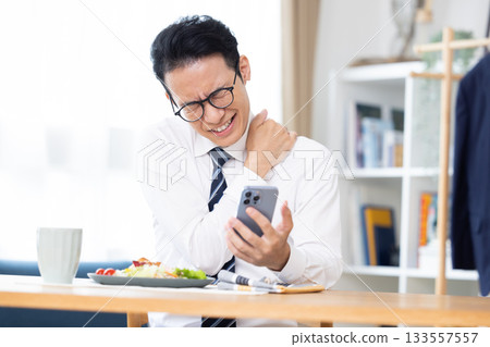 A man eating while looking at his smartphone before going to work A man eating while looking at his smartphone before going to work 133557557