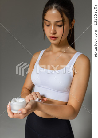 Close-up of a woman applying moisturizing cream to her arm, demonstrating a nourishing skincare step with a jar of body lotion on a neutral background. Close-up of a woman applying moisturizing cream to her arm, demonstrating a nourishing skincare step with a jar of body lotion on a neutral background. 133558205
