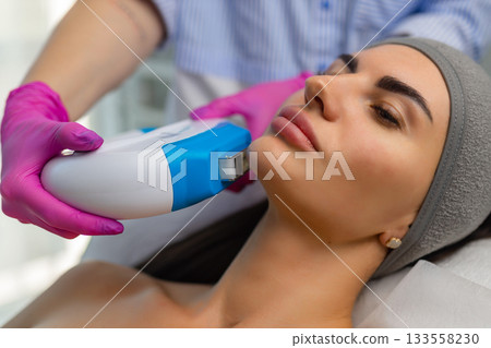 Woman receiving IPL facial treatment with a professional using a handheld device in a beauty clinic. 133558230