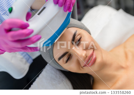Woman receiving IPL facial treatment with a professional using a handheld device in a beauty clinic. 133558260