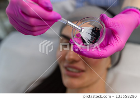 Applying a carbon mask on a woman face with a brush during a carbon laser facial preparation in a beauty clinic. Applying a carbon mask on a woman face with a brush during a carbon laser facial preparation in a beauty clinic. 133558280
