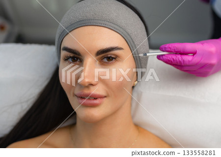Close up of hands of young cosmetologist injecting botox in female face. She is standing and smiling. The woman is closed her eyes with relaxation Close up of hands of young cosmetologist injecting botox in female face. She is standing and smiling. The woman is closed her eyes with relaxation 133558281