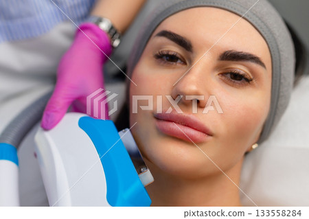 Woman receiving IPL facial treatment with a professional using a handheld device in a beauty clinic. 133558284