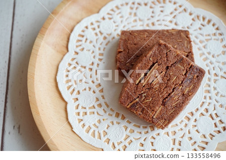 A close-up shot of cocoa cookies arranged on a wooden plate lined with lace paper. 133558496