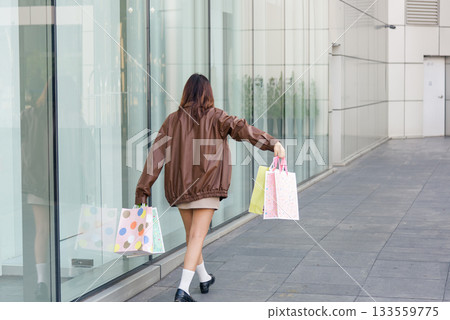 Woman shopping fashion bags, walking from mall, embodies active lifestyle, representing modern consumer culture for people during successful Black Friday shop events. Woman shopping fashion bags, walking from mall, embodies active lifestyle, representing modern consumer culture for people during successful Black Friday shop events. 133559775