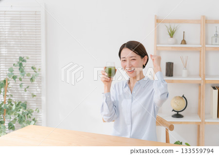 A woman drinking green juice and pumping her fist A woman drinking green juice and pumping her fist 133559794