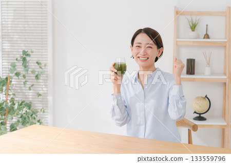 A woman drinking green juice and pumping her fist A woman drinking green juice and pumping her fist 133559796