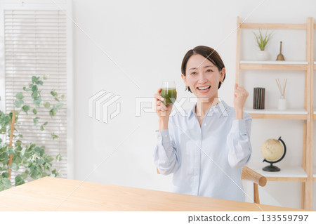 A woman drinking green juice and pumping her fist A woman drinking green juice and pumping her fist 133559797