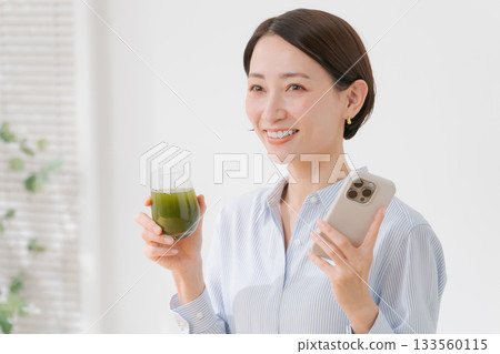 一位女士手捧綠色果汁和一部智慧型手機 133560115