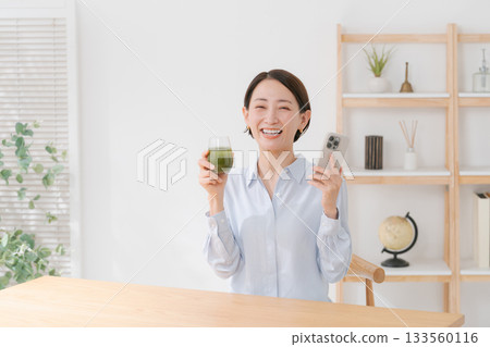 一位女士手捧綠色果汁和一部智慧型手機 一位女士手捧綠色果汁和一部智慧型手機 133560116