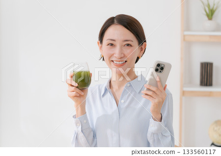 一位女士手捧綠色果汁和一部智慧型手機 133560117