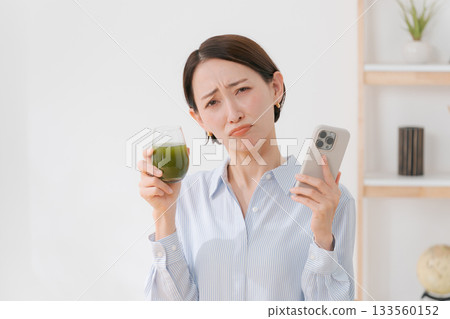 A woman with green juice and a smartphone A woman with green juice and a smartphone 133560152