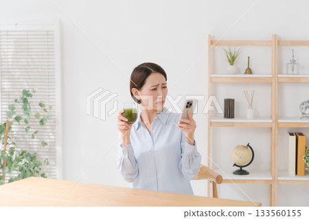 A woman with green juice and a smartphone A woman with green juice and a smartphone 133560155