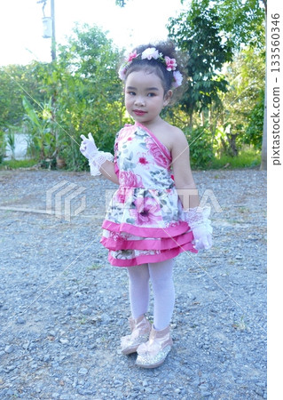 Cute Asian little girl in a pink dress with a flower in her hair in the park Cute Asian little girl in a pink dress with a flower in her hair in the park 133560346