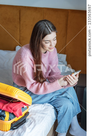 Woman using phone near luggage in hotel room 133563697