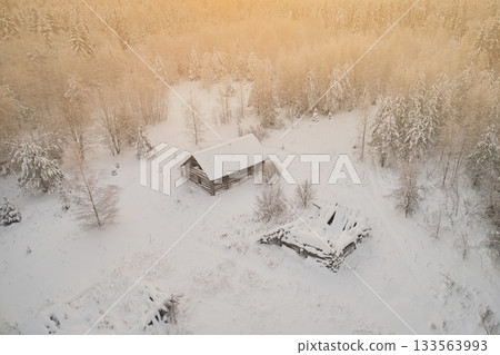 Aerial view of an abandoned village in the forest with destroyed houses against the backdrop of snow and winter landscape. Warm sunset color 133563993