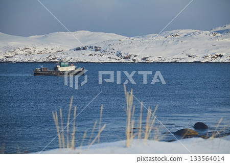 Winter landscape: a ship in the frozen Barents Sea against the background of snow hills and blue sky during the day 133564014