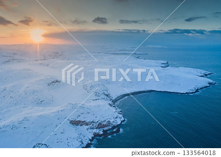 Aerial view of the non-freezing Barents Sea on the Kola Peninsula in winter against the sunset sky and the sun Aerial view of the non-freezing Barents Sea on the Kola Peninsula in winter against the sunset sky and the sun 133564018