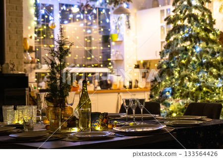 Festive interior of house is decorated for Christmas and New Year in loft style with black stove, fireplace, Christmas tree. Warm studio room with set table, burning wood, cozy and heating of home 133564426
