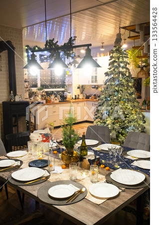 Festive interior of house is decorated for Christmas and New Year in loft style with black stove, fireplace, Christmas tree. Warm studio room with set table, burning wood, cozy and heating of home Festive interior of house is decorated for Christmas and New Year in loft style with black stove, fireplace, Christmas tree. Warm studio room with set table, burning wood, cozy and heating of home 133564428
