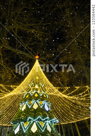High city Christmas tree with a mushroom cap made of garlands, glows at night on the street. Christmas, New Year, decoration of the city. 133564442
