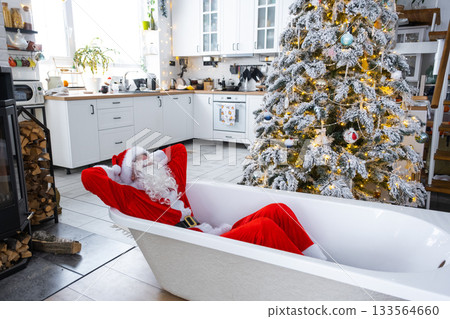 Santa is lying resting in New bathtub under festive Christmas tree as New Year's gift in interior of white modern decorated kitchen. Interior renovation and design, construction and home improvement Santa is lying resting in New bathtub under festive Christmas tree as New Year's gift in interior of white modern decorated kitchen. Interior renovation and design, construction and home improvement 133564660