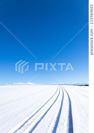 冬日北海道美瑛山區的公路，藍天白雲，積雪壓實的路面上留有汽車的痕跡。 133564683