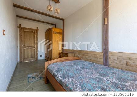 Small Cozy Bedroom Interior with Wooden Furniture and Patterned Bedspread Small Cozy Bedroom Interior with Wooden Furniture and Patterned Bedspread 133565119