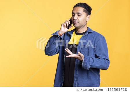 Indian man discussing with best friend over telephone call using his phone. Cheerful ecstatic person talking with people on the telecommunications line using smartphone, studio background. 133565718