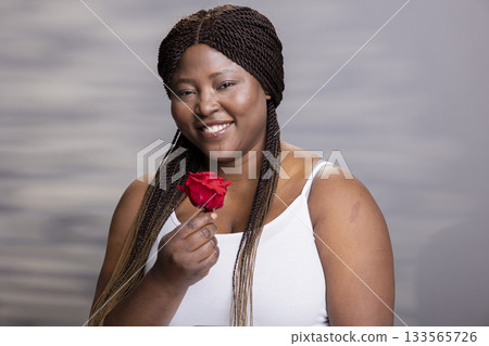 African american female model posing with a red rose and natural look in studio, smooth glossy skin captured in authentic portrait. Her joyful energy and natural look are perfect for self care African american female model posing with a red rose and natural look in studio, smooth glossy skin captured in authentic portrait. Her joyful energy and natural look are perfect for self care 133565726