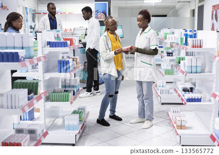 Pharmacy retail worker showing the benefits of health products to woman customer, explaining dosage during a detailed pharmacy visit focused on pharmaceutical care and wellness. Pharmacy retail worker showing the benefits of health products to woman customer, explaining dosage during a detailed pharmacy visit focused on pharmaceutical care and wellness. 133565772