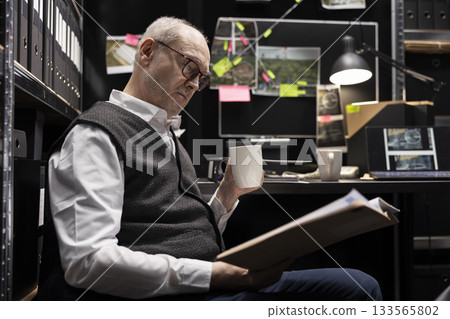 Senior law agent examining evidence and surveillance photos in incident room, working on a criminal case and identifying suspects through tracing clues from multiple documents. 133565802