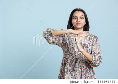 Portrait of assertive indian woman asking for timeout doing hand gestures, feeling fatigued and overworked. Young person gesturing and wishing for a break against studio background. 133565815