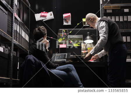 Detective officers study surveillance photos on a mystery board, using investigative tools to trace criminal activity and uncover proof. Identifying a suspect responsible for illegal operation. 133565855