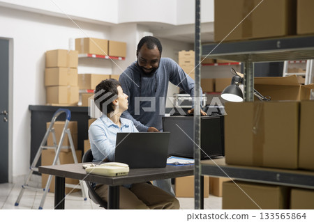 Multiethnic staff collaborates in order processing storage room, surrounded by packages and technology systems in a modern inventory depot designed for small scale distribution services. 133565864