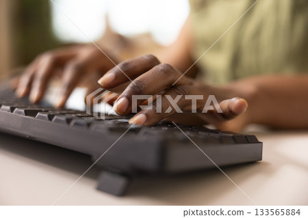 Close up on fingers of african american woman using keyboard to input information on computer. Black female hands on keys, typing data into desktop pc and remotely updating business reports. 133565884