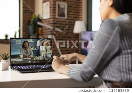 Focused female manager engages in online discussion from home, addressing workplace concerns through laptop video conference with distant coworkers. Virtual meeting among diverse professionals. Focused female manager engages in online discussion from home, addressing workplace concerns through laptop video conference with distant coworkers. Virtual meeting among diverse professionals. 133565889
