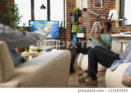 Excited black man cheers with friends over gaming victory at home during casual hangout. Television shows You Win message as joyful individuals celebrate, enjoying video games and fun weekend indoors. Excited black man cheers with friends over gaming victory at home during casual hangout. Television shows You Win message as joyful individuals celebrate, enjoying video games and fun weekend indoors. 133565895