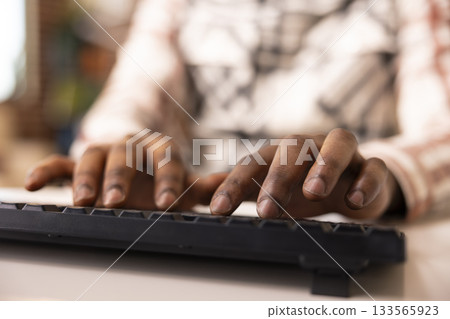 Closeup of male hands using keyboard to draft business emails and prepare marketing documents. African american individual working remotely, types on computer keys, writing content for blog post. 133565923