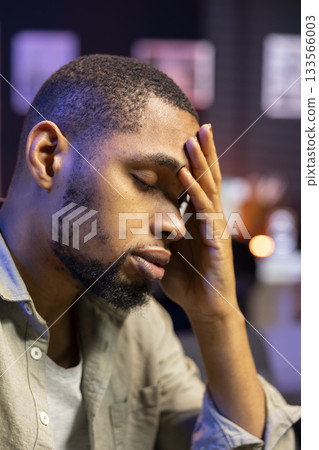 Concerned african american man struggling with task deadlines and work pressure, being stressed and worried about his future. Frustrated scared person working remotely on the couch. Concerned african american man struggling with task deadlines and work pressure, being stressed and worried about his future. Frustrated scared person working remotely on the couch. 133566003
