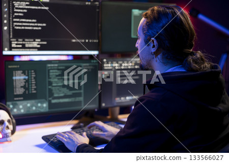 Hacker in neon lit criminal den coding malware designed to exploit network backdoors. Rogue engineer typing on keyboard, bypassing security measures such as logins and password protections 133566027