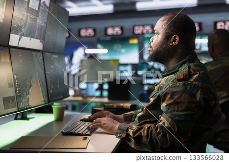 Combat specialist working in governmental facility operating as surveillance monitoring center filled with digital equipment. Intelligence corps doing job in base of operations 133566028