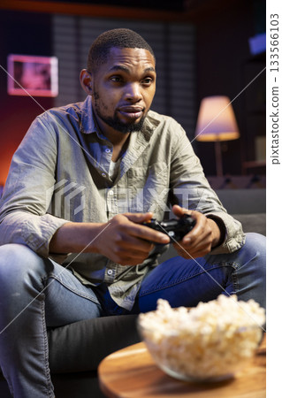 Young guy having fun with video games on television modern setup, connecting his console on smart tv in living room and enjoying chill game night at home. African american gamer playing tournament. Young guy having fun with video games on television modern setup, connecting his console on smart tv in living room and enjoying chill game night at home. African american gamer playing tournament. 133566103